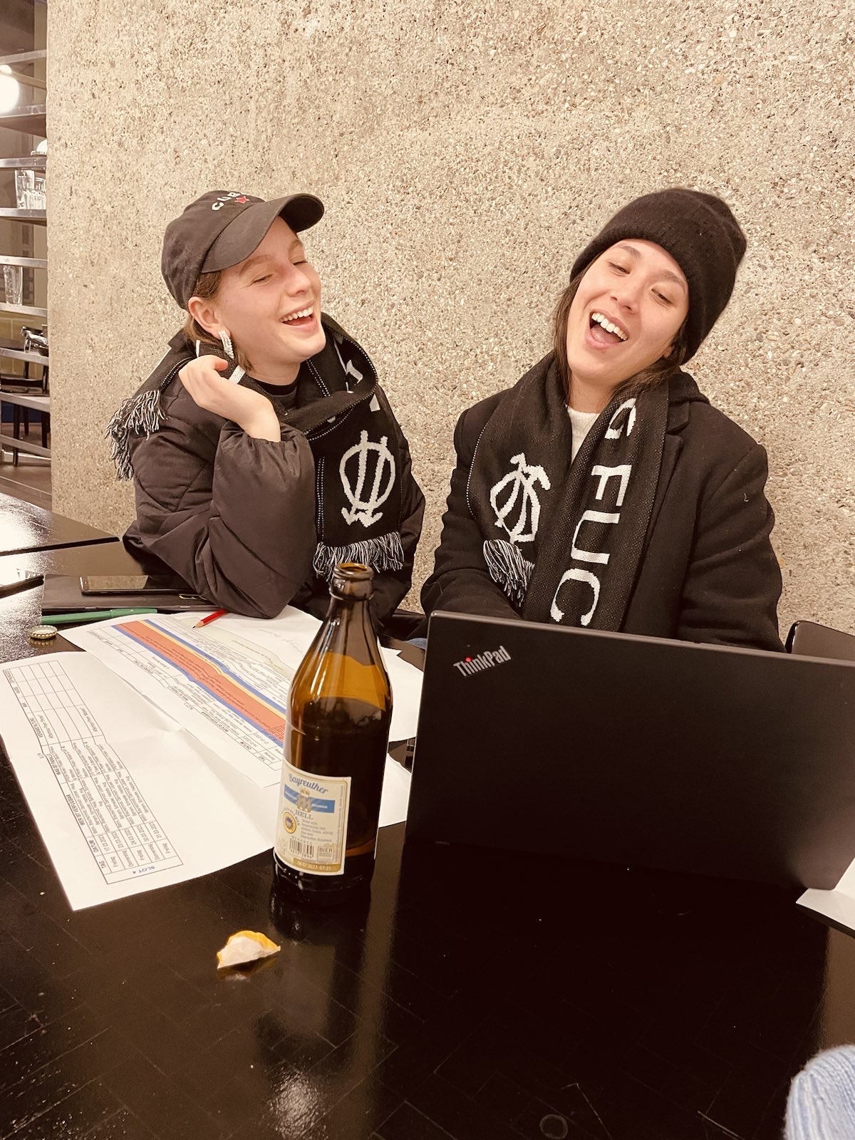 Zwei Personen sitzen lachend vor einem Laptop und einem Bier